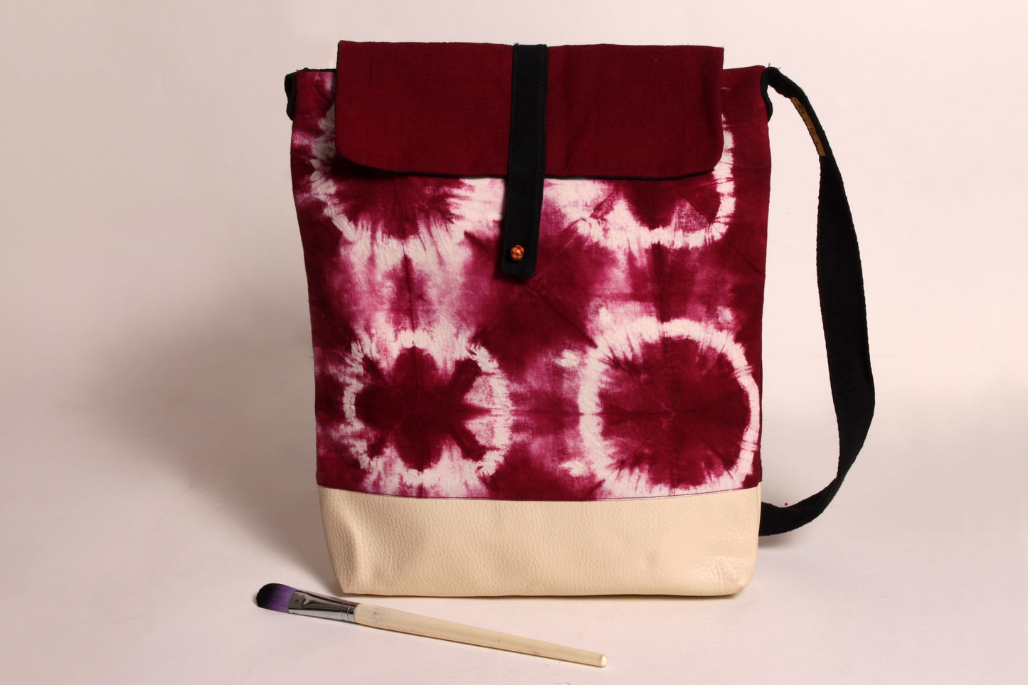 Front view of Maroon Flower Artist Bag made from cotton fabric with faux leather, a magnetic snap closure, and a pocket 